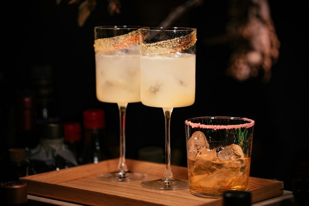Three crafted drinks with seasoned rims and ice on a wooden tray