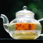 Glass teapot holding pale botanical tea and an orange flower