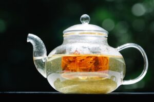 Glass teapot holding pale botanical tea and an orange flower