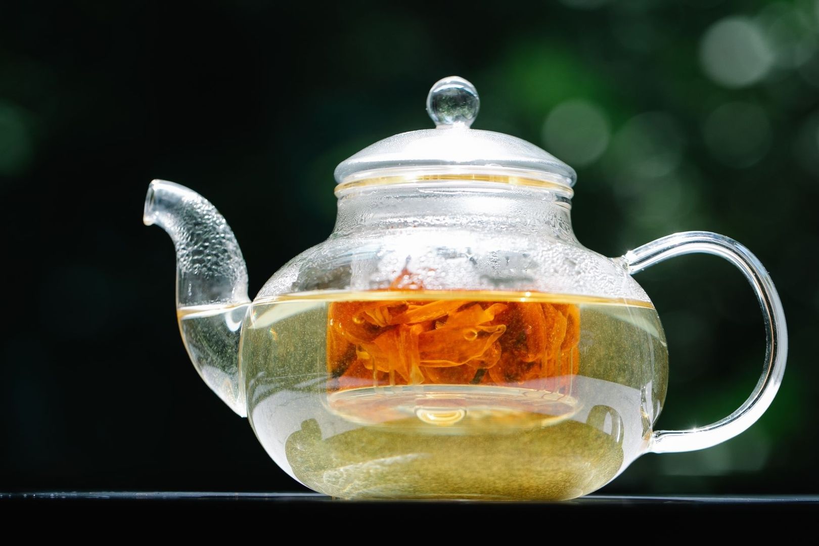 Glass teapot holding pale botanical tea and an orange flower